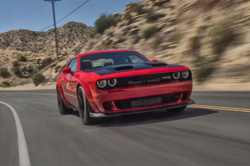 A red 2023 Dodge Challenger SRT Jailbreak being driven on a curved highway with the background blurred to indicate the speed of the vehicle.
