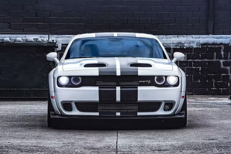 A white 2023 Dodge Challenger SRT Hellcat with black center stripes, parked in an alley.