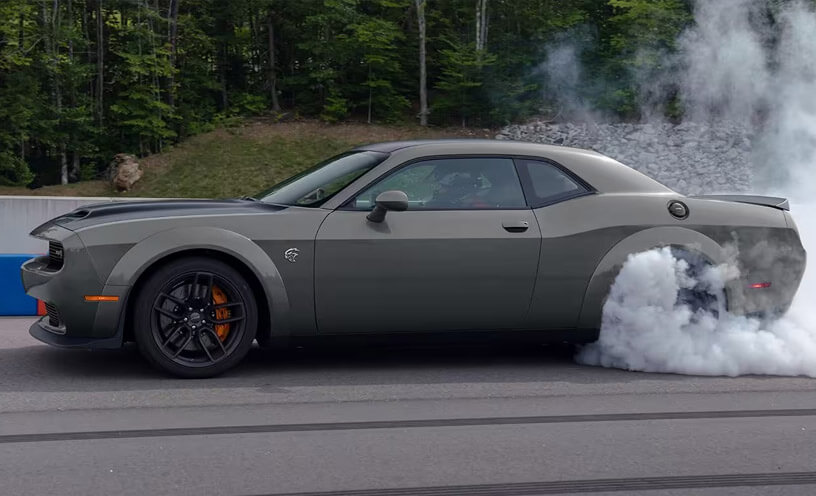 A driver-side profile of a gray 2023 Dodge Challenger R/T Scat Pack Widebody with the Swinger Special Edition Appearance Package on a track with smoke billowing from its rear tires.