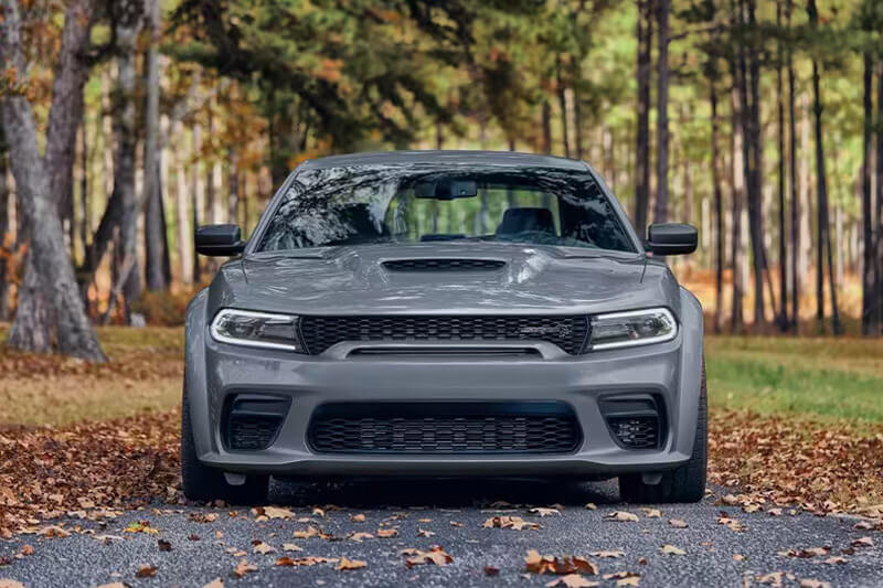 A head-on angle of a gray 2023 Dodge Charger SRT Hellcat parked on a road in the woods.