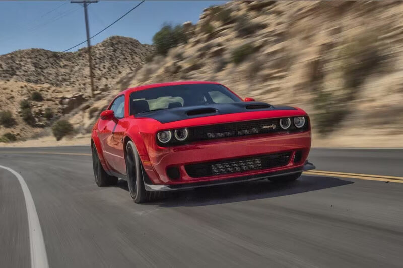 A red 2023 Dodge Challenger SRT Jailbreak being driven on a curved highway with the background blurred to indicate the speed of the vehicle.